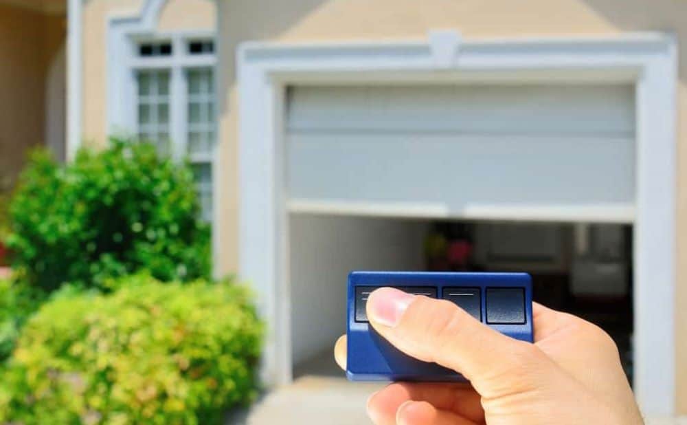 White Hand Pressing Left Button on Three-Button Garage Door Opener to Lift One-Car Garage-min