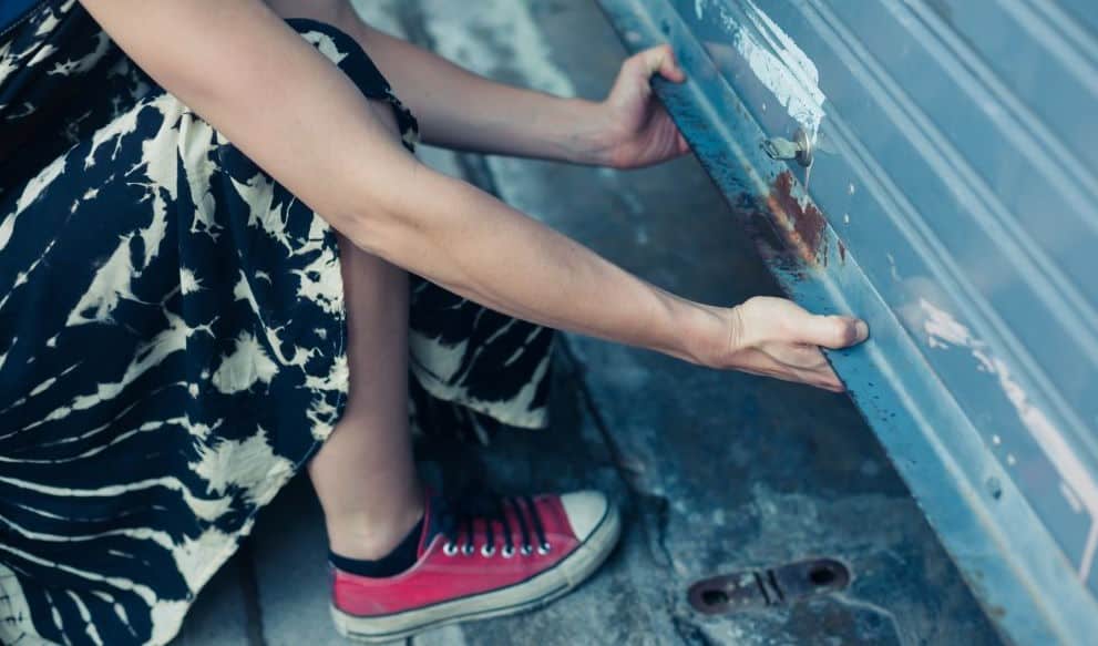 A woman in a dress and pink shoes manually opening garage door with broken spring